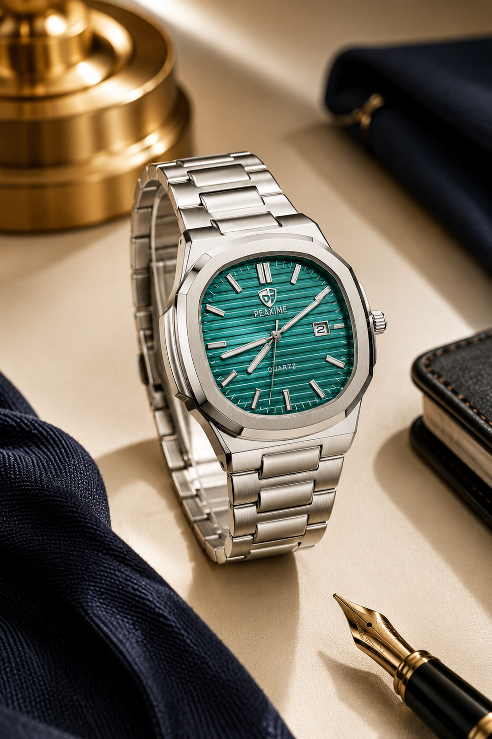 Silver watch with green face on a light surface with a pen and fabric
